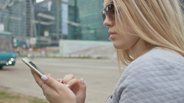 Girl typing on a phone against the background of high-rise buildings in the center of the city.