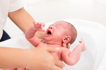 Little newborn baby crying while being taken a bath