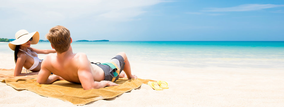Couple lying on white sand beach relaxing and taking a sunbath in summer