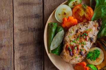 Homemade chicken breast barbecue on wood plate served with grilled vegetables. Delicious chicken barbecue and grilled vegetables for lunch or dinner. Roast chicken breast on rustic wood table.