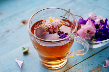 Cup of tea and branch of small pink roses on rustic table.