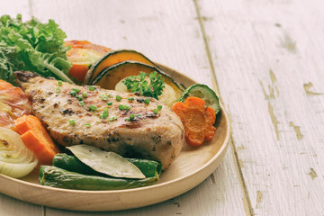 Homemade chicken breast barbecue on wood plate served with grilled vegetables. Delicious chicken barbecue and grilled vegetables for lunch or dinner. Roast chicken breast on rustic wood table.