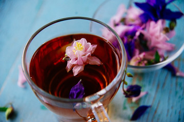 Cup of tea and branch of small pink roses on rustic table.