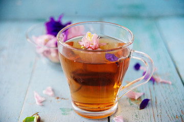 Cup of tea and branch of small pink roses on rustic table.