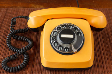 Close up of an old, scratched orange rotary dial telephone