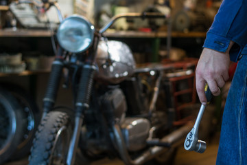 Man's hand holding a socket metal wrench with ratchet in the garage, on the background of motorcycle