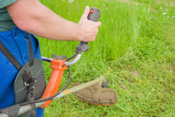 Man wearing overalls mowing green grass with gasoline lawn trimmer. The differences between the...