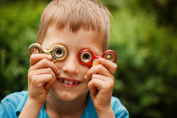 Cute little boy playing with fidget hand spinner in summer day. Popular and trendy toy for children and adult. - obrazy, fototapety, plakaty