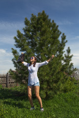 Beautiful young businesswoman of European appearance with a briefcase in her hands is happy and jumping near cedar or pine. Summer sunny day in nature.
