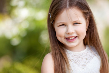 Beautiful smiling little girl in cream dress, against green of summer park © fadzeyeva