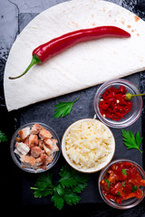 Ingredients for mexican quesadilla with salsa on black slate stone plate. Top view.