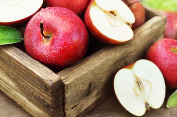Crate of fresh ripe harvested red apples with leaves on wooden background, selective focus