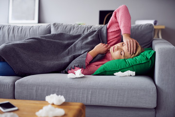 Sick woman holding her head while lying in bed under blanket