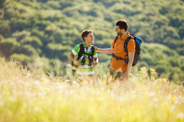 Father and son are hiking in nature in summer. They are using binoculars.