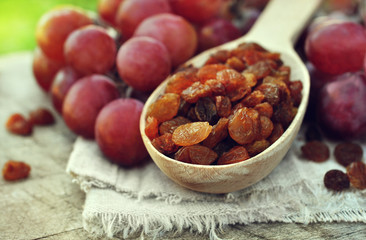 Dried red raisins in wooden spoon with fresh ripe grapes