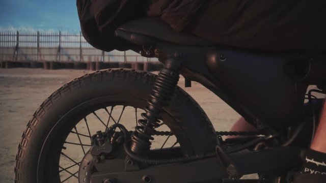 Close up dolly shot of motorcyclist and his motorbike on the beach during sunset