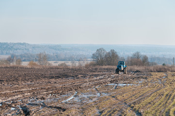 Wheeled tractor comes towards on dirt road in fallow field
