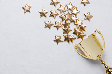 Golden winner trophy cup with golden stars on white textured background with copy-space