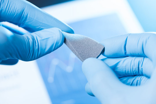 Scientist hand in gloves hold and bend small piece of gray porous foam, new type of material with different properties research concept