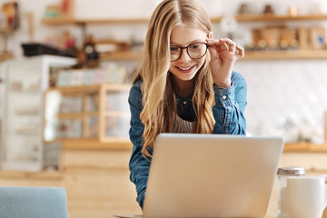 Pretty teenage girl working on laptop and adjusting glasses