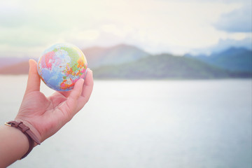 The hand holds a model globe and has a mountain and river background. Travel Concept. Communication and Technology Concept. Business Concept.