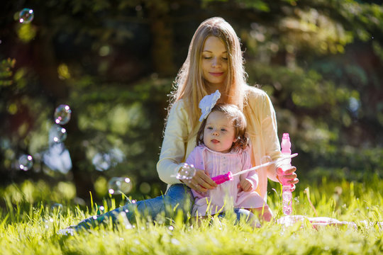A young mother with her daughter blowing soap bubbles in the park
