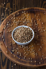 Buckwheat grain on ceramic bowl over wooden table.