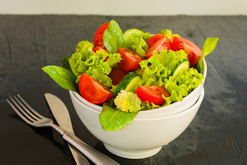 Lettuce leaves, cherry tomatoes, cucumber and broccoli salad on dark background.