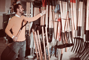 Naklejka premium Man choosing new shovel in garden equipment shop