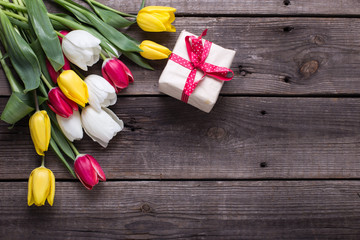 Bright yellow, pink  and white tulips flowers  and gift in wrapped box on  vintage wooden background.