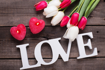 Word love, two red  candles in form of heart  and  bright spring flowers on wooden background.