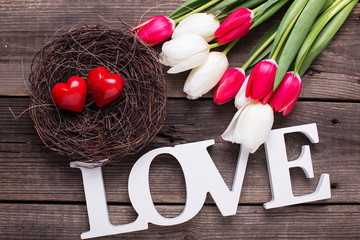 Word love, two red hearts in nest and  bright spring flowers on wooden background.