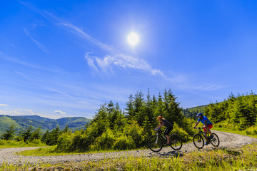 Fototapeta na wymiar Mountain biking women and man riding on bikes in early spring mountains forest landscape. Couple cycling outdoor sport activity.