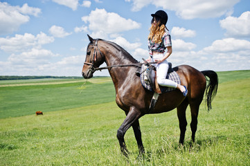 Young pretty girl riding a horse on a field at sunny day.