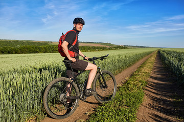 Young cyclist standing with mountain bike on background of beautiful landscape.