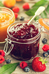 Tasty fruit red strawberry berry jams in glass jar with fruits on wooden table. Closeup.