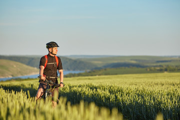 Attractive cyclist stands on the bike on the trail of the hay field in summer season.