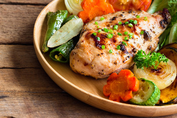 Homemade chicken breast barbecue on wood plate served with grilled vegetables. Delicious chicken barbecue and grilled vegetables for lunch or dinner. Roast chicken breast on rustic wood table.