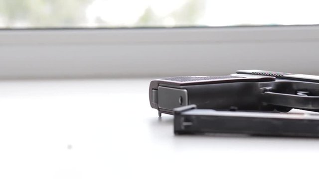 A military pistol on a white window sill, sunlight from a window
