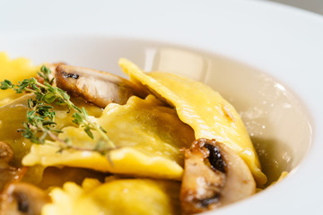White plate with freshly prepared pasta ravioli and fried champignons mushrooms cut into slices. The dish is decorated with a sprig of rosemary. Traditional Italian homemade food. Macro Closeup.