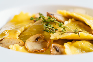White plate with freshly prepared pasta ravioli and fried champignons mushrooms cut into slices. The dish is decorated with a sprig of rosemary. Traditional Italian homemade food. Macro Closeup.