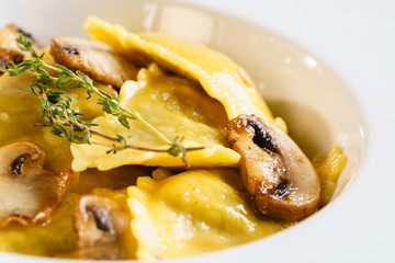 White plate with freshly prepared pasta ravioli and fried champignons mushrooms cut into slices. The dish is decorated with a sprig of rosemary. Traditional Italian homemade food. Macro Closeup.