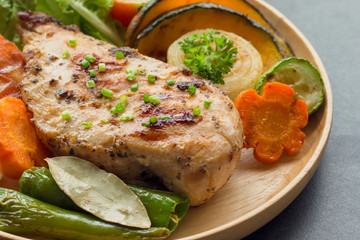 Homemade chicken breast barbecue on wood plate served with grilled vegetables. Delicious chicken barbecue and grilled vegetables for lunch or dinner. Roast chicken breast on granite table.