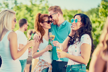 Group of best friends chatting and drinking while standing at outdoor party