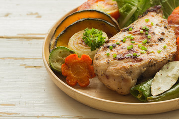 Homemade chicken breast barbecue on wood plate served with grilled vegetables. Delicious chicken barbecue and grilled vegetables for lunch or dinner. Roast chicken breast on rustic wood table.