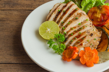 Sliced chicken breast barbecue on white plate served with grilled vegetable. Delicious  chicken breast steak and salad for dinner. Homemade chicken breast barbecue on wood table for background.