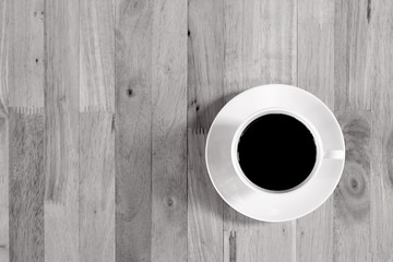 Coffee cup with black coffee on wood table, top view with copy space, monochrome effect