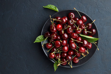 Ripe sweet cherry in black plate on dark stone background.