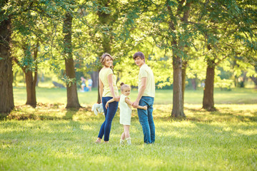 Family standing in summer park. Mother, father and daughter embracing on the grass in nature on a sunny day.