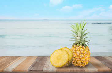 Naklejka na ściany i meble Pineapple on the wooden table with sea and blue sky background.